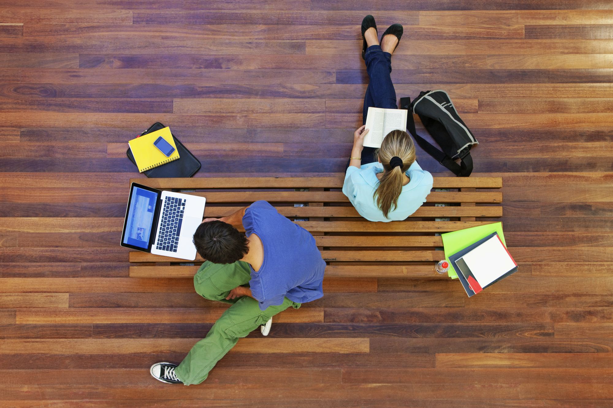 The image shows a young man on the left with a laptop and a young woman on the right with a book.