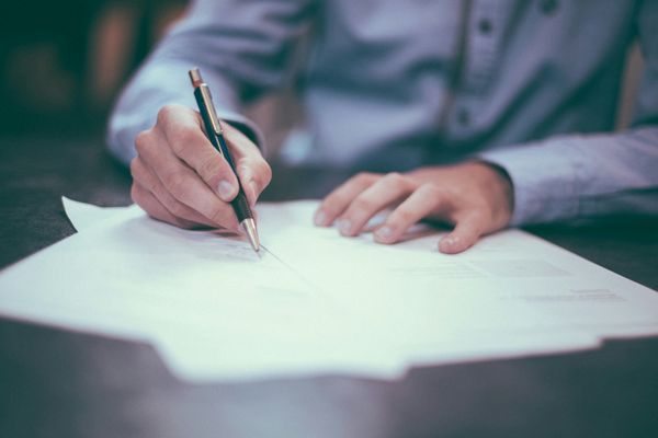 The image shows a man sitting at a table with pen in hand, working on papers. He's illustrative of consulting work.